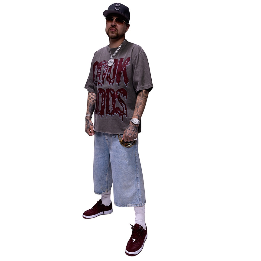 Cook Gods grey cotton t-shirt with dripping logo graphic. Model wears light wash denim shorts and burgundy sneakers.