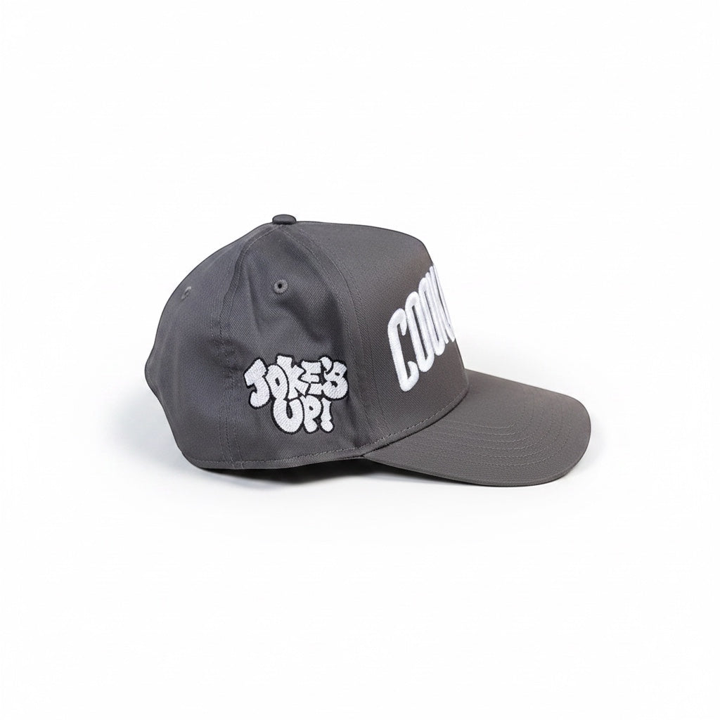 Cook Gods grey snapback cap with white "COOK GODS" logo on front and "JOKE'S UP!" graphic on side.