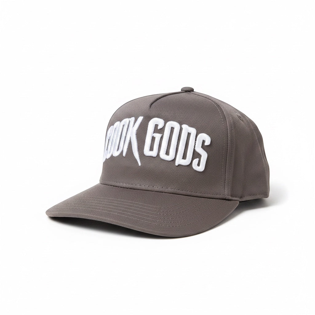 Cook Gods grey snapback cap with white embroidered "COOK GODS" logo on the front and "JOKE'S UP!" graphic on the side.