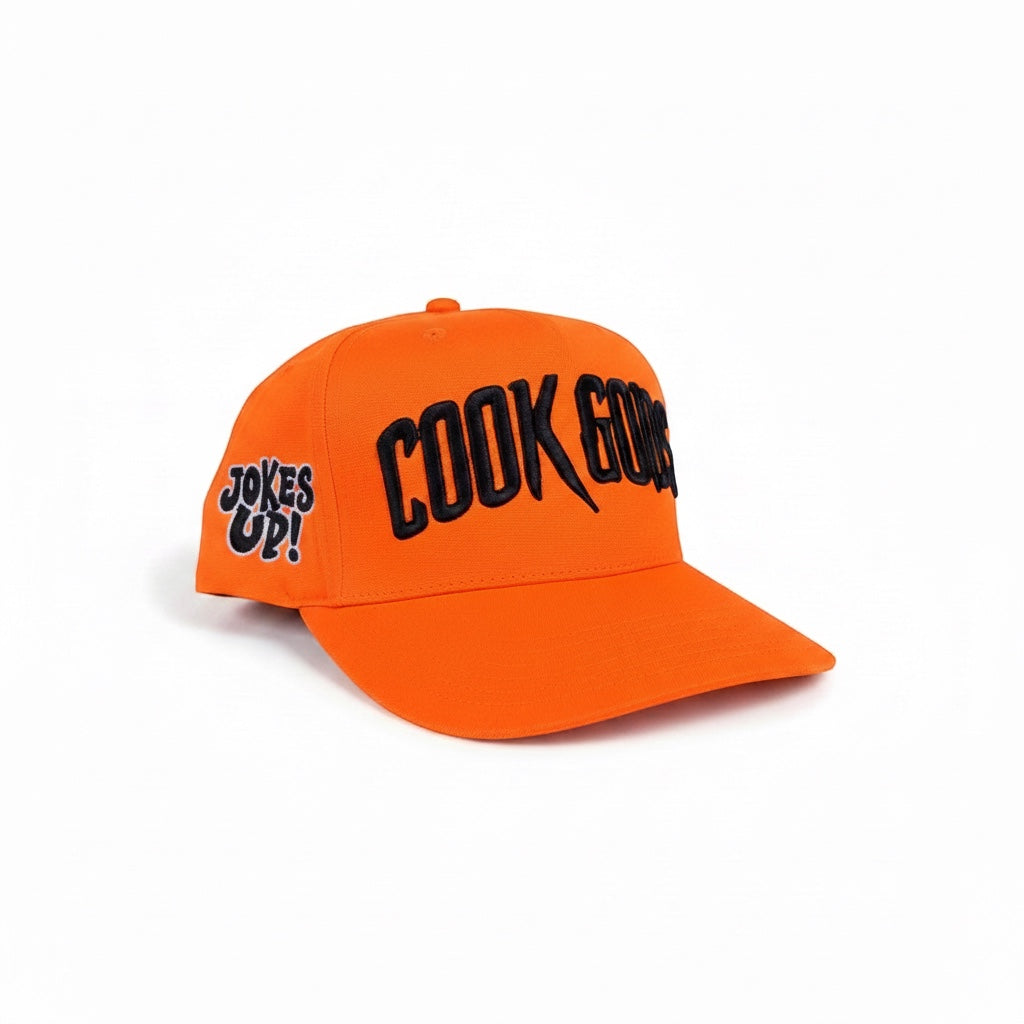 Cook Gods orange snapback hat with black embroidered "COOK GODS" logo on front and "COOK UPPS" on side.