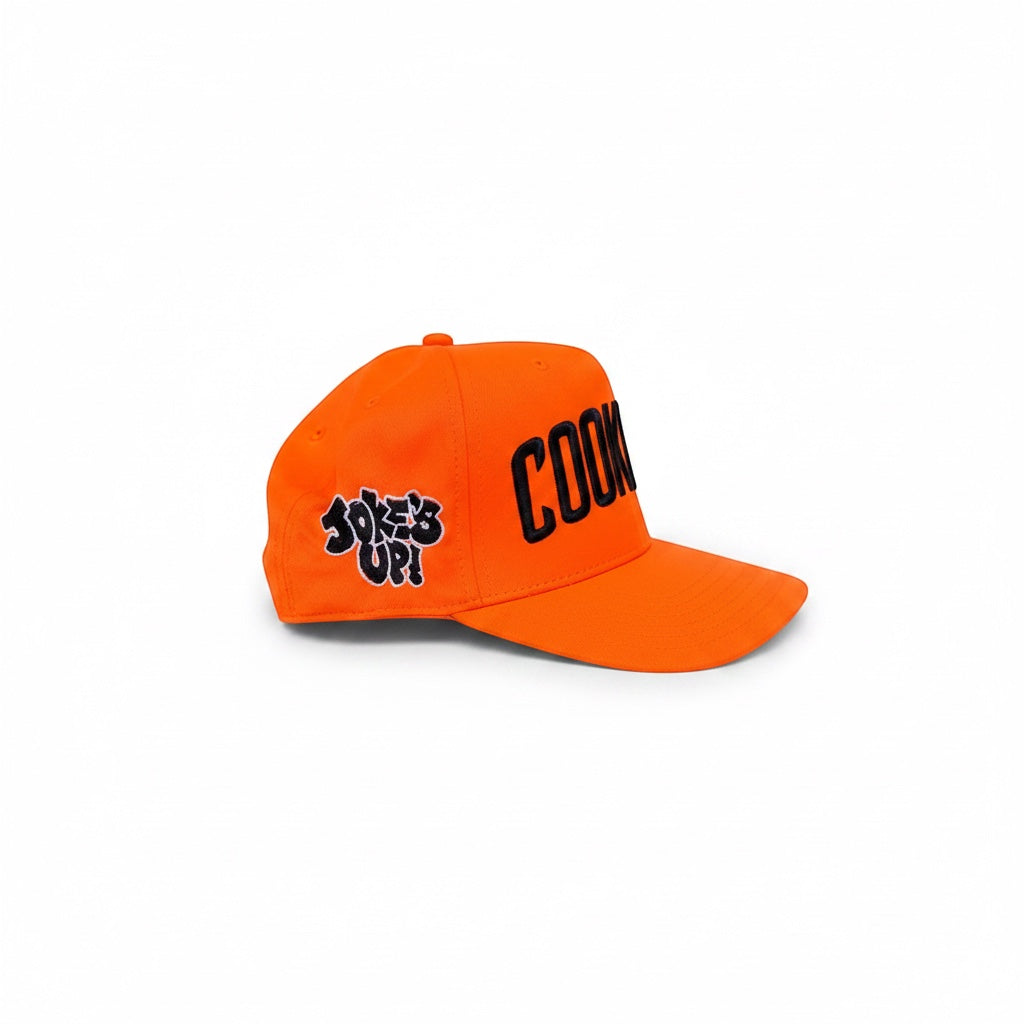 Cook Gods orange snapback hat with black embroidered "COOK" text on the front and "JOKES UP!" on the side.